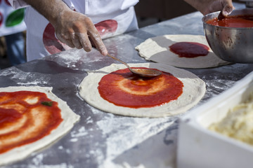 La preparazione di una pizza margherita a Napoli, con il cucchiaio che versa il pomodoro