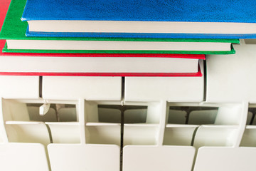 Stack of multicolored books lies on a white radiator