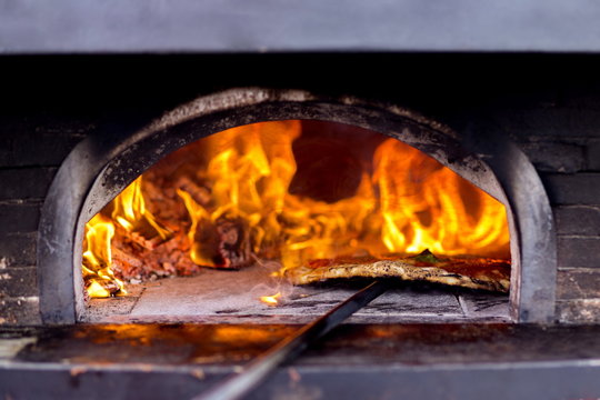 Una pizza che sta venendo infornata in un forno a Napoli, con sfondo di fuoco
