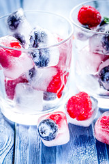 glass with frozen berries in cubes on wooden desk background