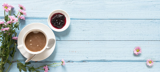 Fototapeta na wymiar Coffee cup, jam and pink flowers on a pastel blue wooden background with copy space, top view from above, panoramic banner format