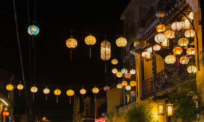 Colourful orange and yellow fabric lanterns hang across a street in the historic UNESCO listed Vietnamese town of Hoi An.
