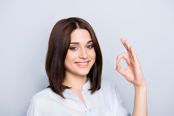 Close up portrait of stylish, charming, attractive, pretty, nice, caucasian, brunette woman with modern hairstyle, showing ok symbol with fingers, looking at camera, isolated on grey background