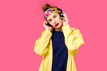 Young beautiful woman on a pink background and a yellow coat listening to music through wireless headphones. Concept of healthy nutrition and sports.  Colour obsession concept.