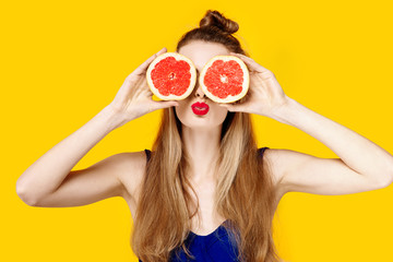 Young woman on a yellow background and a blue dress is holding a cut orange in her hands. Concept of healthy nutrition and sports.  Colour obsession concept.  Minimalistic style. Stylish Trendy