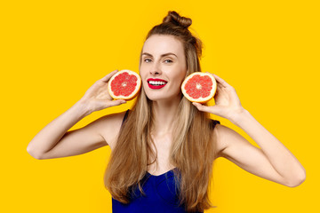 Young woman on a yellow background and a blue dress is holding a cut orange in her hands. Concept of healthy nutrition and sports.  Colour obsession concept.  Minimalistic style. Stylish Trendy