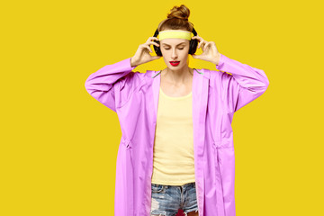 Obraz premium Young woman on a yellow background and a pink coat hugs music worm wireless headphones. Colour obsession concept. Minimalistic style. Stylish Trendy