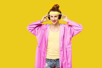 Young woman on a yellow background and a pink coat hugs music worm wireless headphones. Colour obsession concept.  Minimalistic style. Stylish Trendy