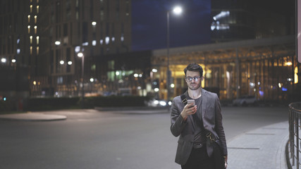 Fototapeta na wymiar A young man is holding scrolling texting in his cellphone. A man waiting for a taxi in night time