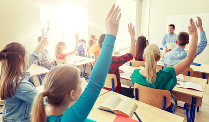 education, high school, teaching, learning and people concept - group of happy students raising hands and teacher in classroom