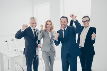 Portrait of attractive, lucky, stylish business people in suits celebrating victory in tender, successfully completed project with raised hands, looking at camera, standing on work place, station