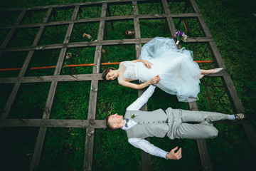 beautiful fabulous happy bride and stylish groom lying down on the grass on the background of the sunny stunning mountains