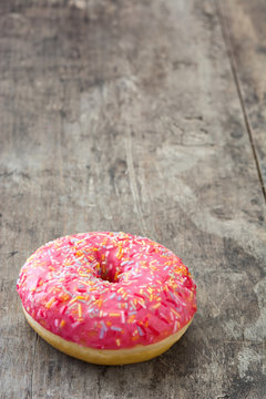 Pink frosted donut with colorful sprinkles on wooden table