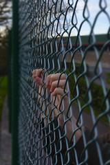 Hands of a refugee woman on a wire fence, a girl imprisoned and deprived of freedom