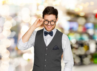 fashion, style and vintage concept - happy man in festive suit and eyeglasses over holidays lights...
