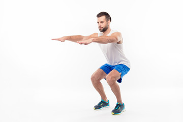 Full-length, half turned portrait of active, sporty, attractive person making, doing squats with straight arms, hands forward, isolated on white background