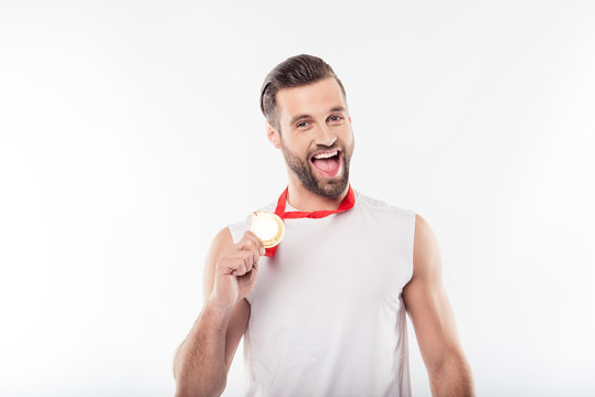 It is mine! Lucky, attractive, powerful, sporty, athletic, strong, cheerful, positive man having gold medal with red ribbon on his neck, showing trophy with hand, yelling over white background
