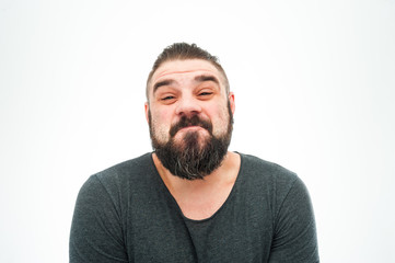Obraz premium Good looking cute young bearded male looks with hesitant expression as doubts what to choose, points with thumb aside, copy space for promotional text or advertisment