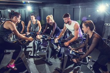 Group of sporty people with personal trainer  exercising together during cycling class in gym