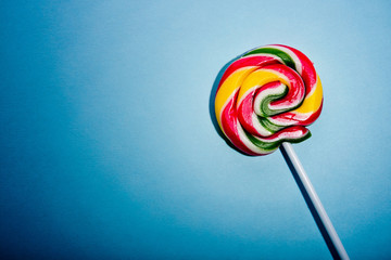 Colorful spiral lollipop candy on stick. On a blue background.
