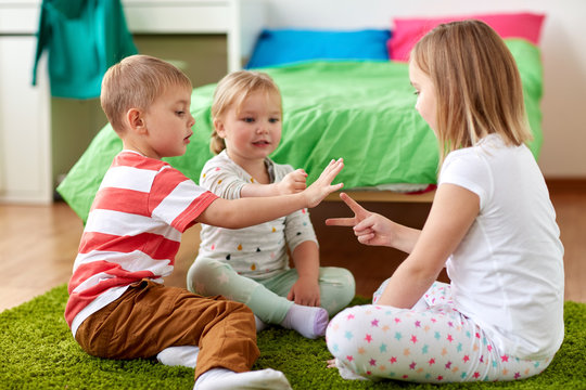 childhood, leisure and family concept - happy little kids playing rock-paper-scissors game at home
