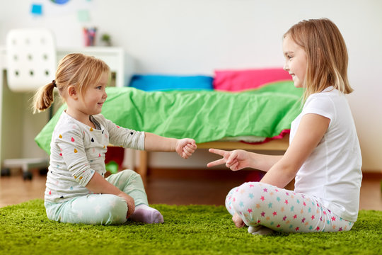 childhood, leisure and family concept - happy little girls playing rock-paper-scissors game at home