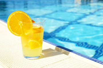 Close up of screwdriver cocktail alcohol drink with orange juice, slices and ice standing near the pool. Refreshing iced lemonade beverage in glass by the poolside. Sun glares. Background, copy space.