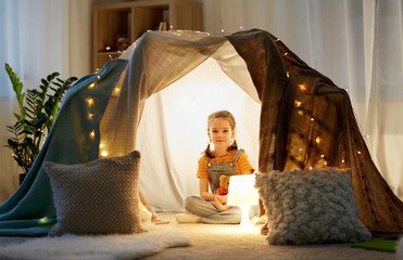 childhood and hygge concept - happy little girl with toys in kids tent at home