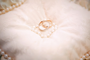 Wedding rings on a white cushion with pearls. Wedding symbol.