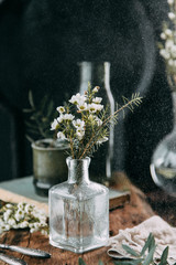 Spring flowers and greens in the decor on the table, in glass bottles with water and droplets on...