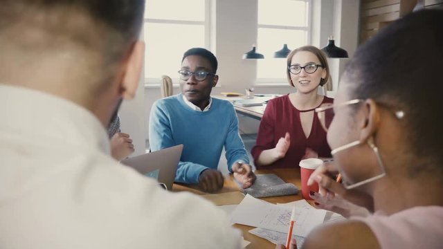 Multi ethnic group at office business meeting. Young diverse partners discuss ideas, then start clapping and smiling 4K.
