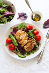 Sliced grilled chicken with green leaves salad on white plate