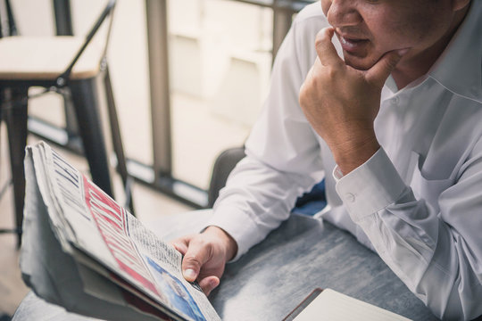 Young businessman sipping coffee and reading newspaper at office.Business man, modern office building with beautiful golden sunlight as background.