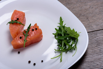 Slices of salmon with arugula on a white plate
