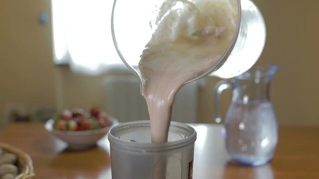 Uomo sta versando il frullato di frutta fresca in un bicchiere di plastica per palestra.