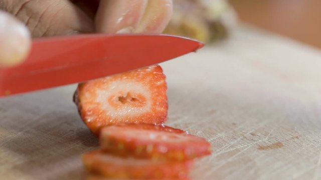 Mano di un uomo che tagliano la fragola con un coltello rosso su un tagliere di legno