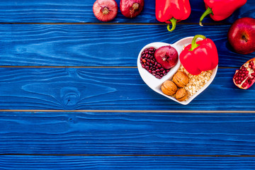 Food which help heart stay healthy. Vegetables, fruits, nuts in heart shaped bowl on blue wooden background top view copy space