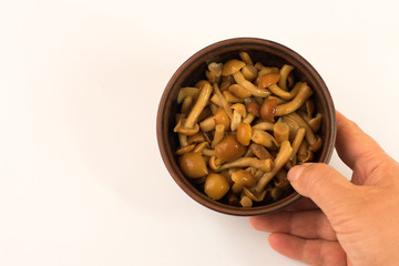 Marinated mushrooms in a bowl in woman's hand on white background