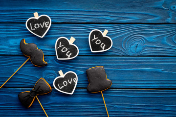 Happy Father's Day. Greetings and presents concept. Cookies in shape of moustache, hat, bow tie and hearts with lettering love you on blue wooden background top view copy space
