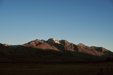 Fototapeta na wymiar Paisaje de picos de montañas nevadas con cielo azul despejado al atardecer en Nueva Zelanda 
