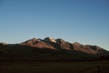 Paisaje de picos de montañas nevadas con cielo azul despejado al atardecer en Nueva Zelanda	