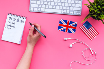 Learn new english vocabulary. Learn landuage concept. Computer keyboard, british and american flags, notebook for writing new vocabulary on pink background top view