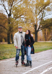 A happy old man laughs and stands on roller skates on the road and hugs his daughter in an autumn park.