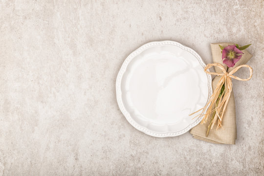 Empty white plate, vintage style linen napkin and purple flowers on stone background. Top view, flat lay and copy space