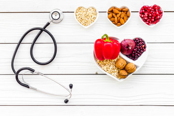 Products good for heart and blood vessels. Vegetables, fruits, nuts in heart shaped bowl near...
