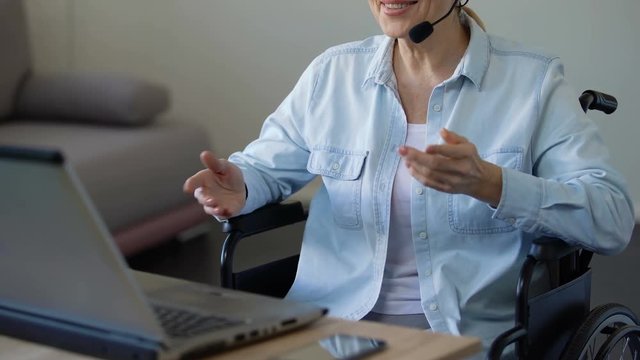 Disabled female consultant with headset talking with client, working on laptop