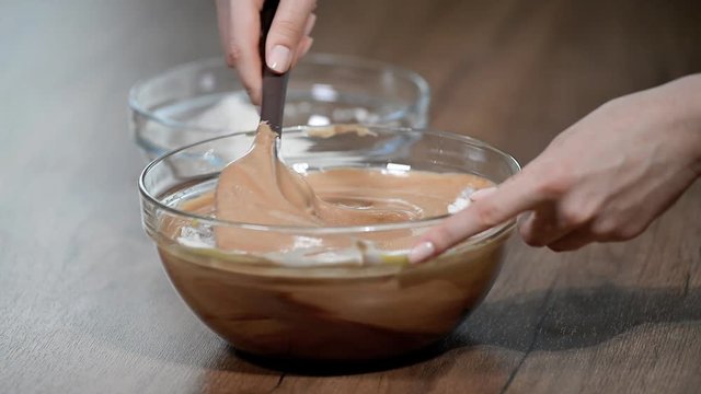 A confectioner cooks a dough. A hand with a plastic spatula stirs the dough in a bowl for baking a chocolate biscuit cake.