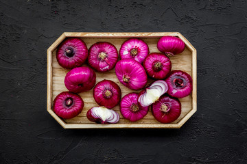 Red onion is healthy product. Onion bulbs in tray on black background top view copy space