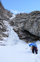 male ice climber approaches  a long and steep waterfall in a narrow frozen couloir in the Alps