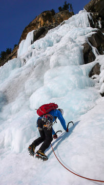 male ice climber in a blue jacket on a gorgrous frozen waterfall climbing in the Alps in deep winter